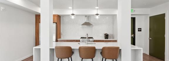 A kitchen with white walls and a wooden island with three chairs.