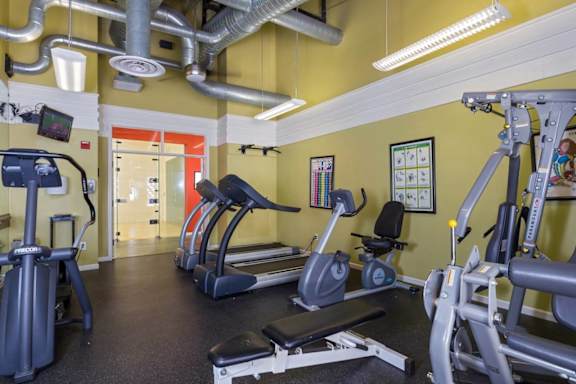 a gym with cardio equipment and weights in a building with yellow walls at Village Club of Royal Oak, Royal Oak