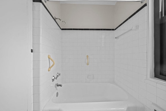 a white tiled bathroom with a tub and a window