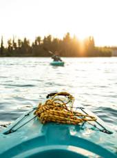 A blue kayak with a yellow rope tied to the front is in the foreground with another kayak in the distance on a body of water.