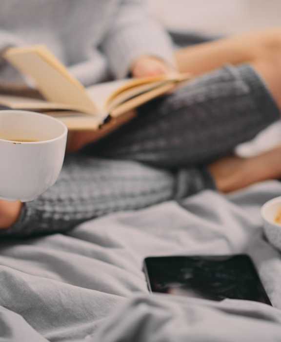 A person is reading a book while holding a cup of coffee.