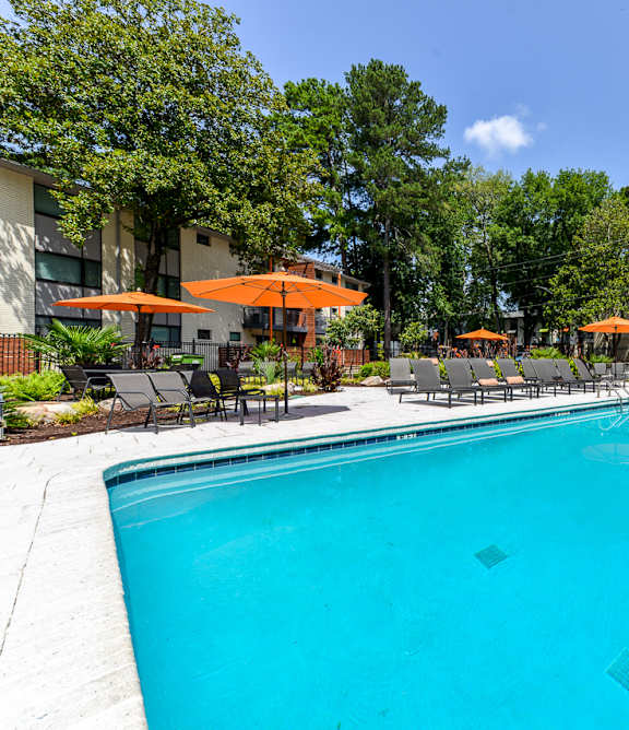 A swimming pool surrounded by trees and chairs.