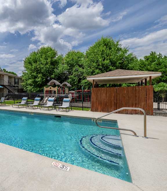 A swimming pool with lounge chairs and a building in the background.