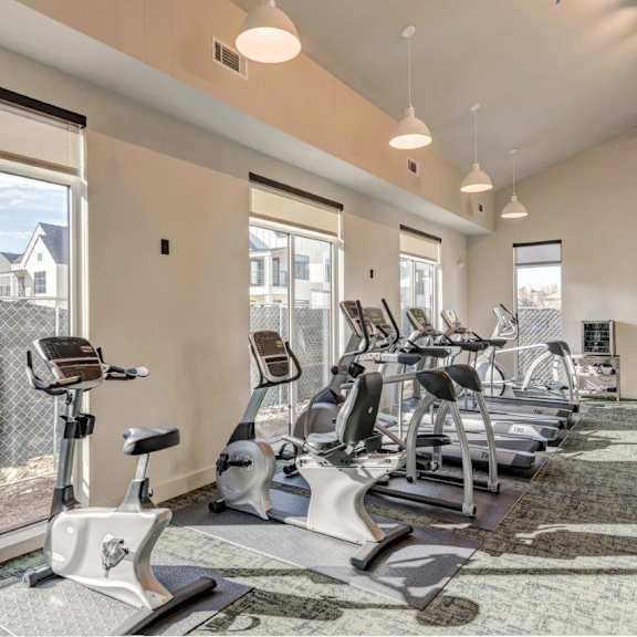 a gym with cardio machines and windows at the district flats apartments in lenexa