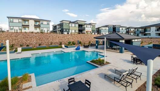 A swimming pool surrounded by a patio with chairs and a building in the background.