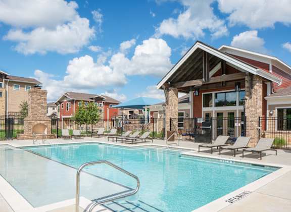A swimming pool surrounded by lounge chairs and buildings in the background.