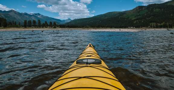 A yellow kayak is in the foreground with a mountainous landscape in the background.