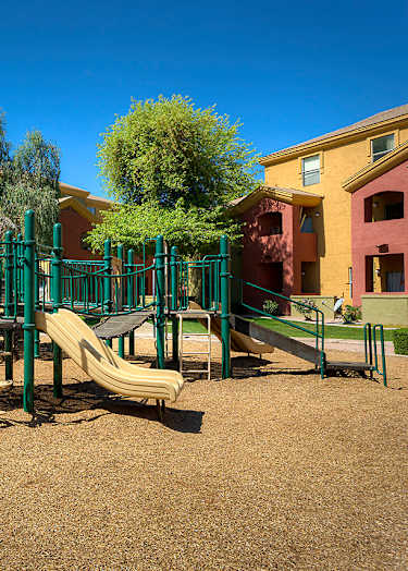 A basketball court with a bench on the side and two houses in the background.