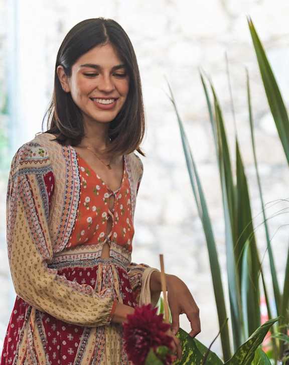 A woman in a patterned dress is standing in front of a flower shop.