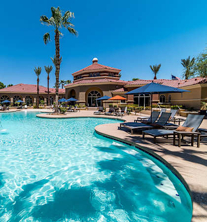 A large swimming pool with a blue tinted water surrounded by palm trees and sun loungers.