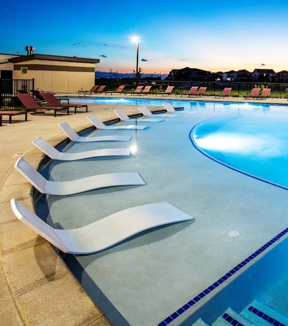 A swimming pool with sun loungers and a building in the background.