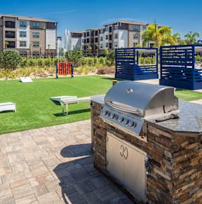 a barbecue grill on a patio with a lawn and apartments in the background