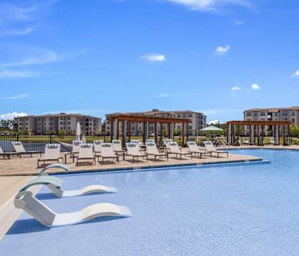 A large swimming pool with lounge chairs and a building in the background.