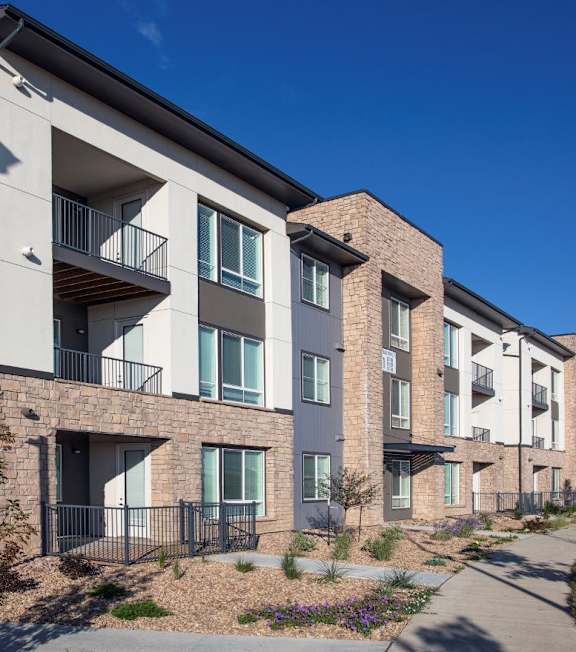 A row of modern apartment buildings with balconies and potted plants in front.