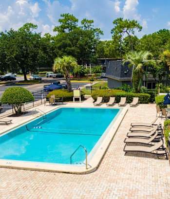 a swimming pool with chaise lounge chairs and trees in the background at Auburn Glen Apartments, Florida, 32256