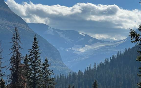 a view of the mountains and trees in the foreground and a blue sky with clouds