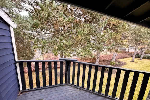 A wooden deck with a black railing overlooks a yard.