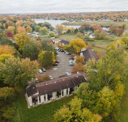 an aerial view of a white building with a brown roof surrounded by trees and a body of