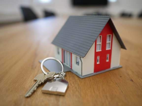 A small model house with a set of keys on a wooden surface.