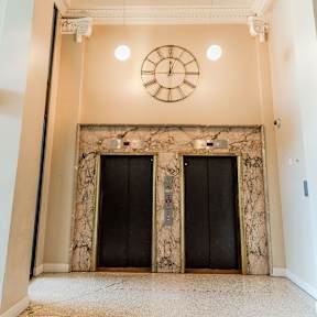 A clock hangs on a wall above two black doors.