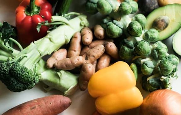 A variety of vegetables including broccoli, carrots, and peppers are displayed on a white surface.