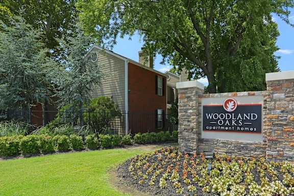 A sign for Woodland Oaks Apartment Homes is in front of a building.