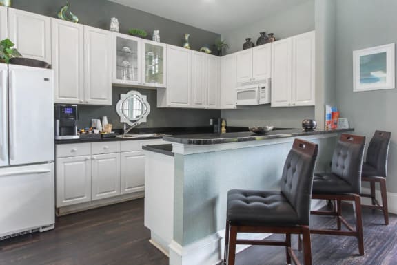 Decorated Clubhouse Kitchen with White Cabinets White Appliances with Black Counters and Brown Bar Stools