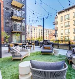 A patio with a white couch and chairs with a black railing and a building in the background.