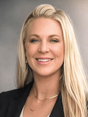 A woman with blonde hair wearing a black blazer and a necklace.