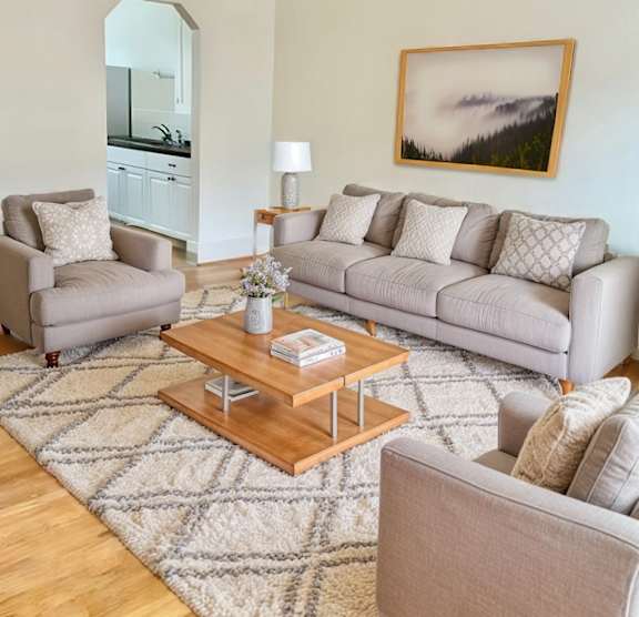 A living room with a grey couch, a grey armchair, a wooden coffee table, and a grey rug.
