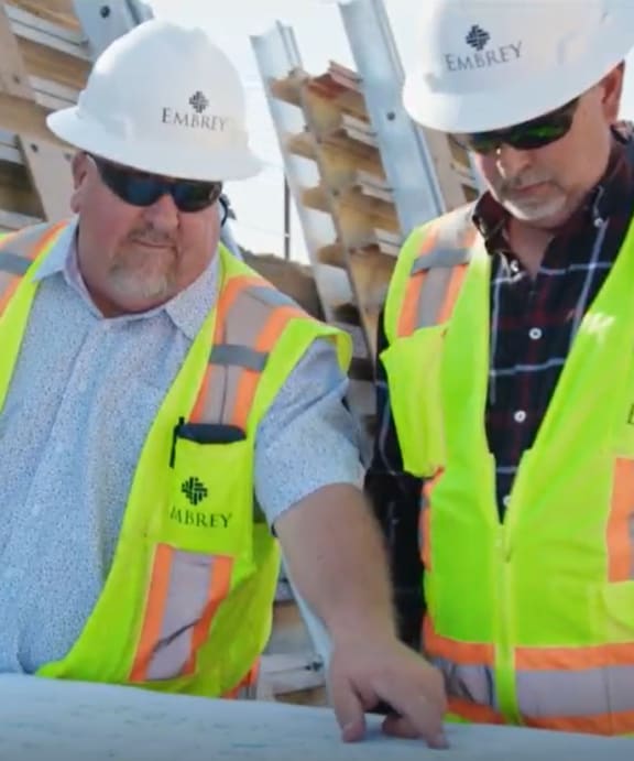 two men wearing construction hats and yellow vests working on a table