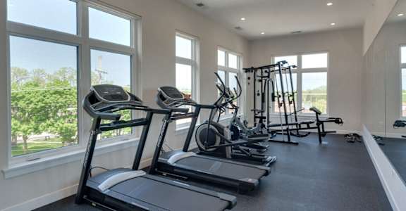 Fitness center at Highpoint Highwood Station 246 apartments with cardio equipment, weights, and large windows