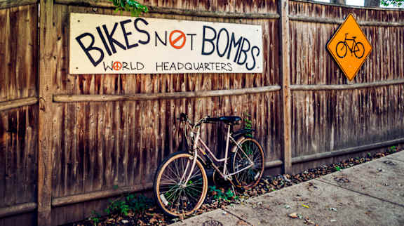 A bicycle is leaning against a wooden fence with a sign that says "Bikes Not Bombs".