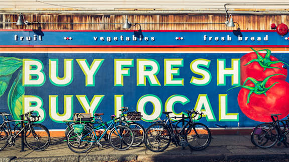 A mural promoting buying fresh and local products with bicycles parked in front.