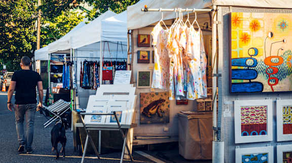 A man walking his dog past a white tent with various items for sale.