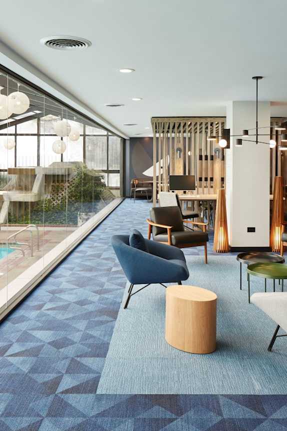 A modern indoor swimming pool area with a blue carpet and chairs.