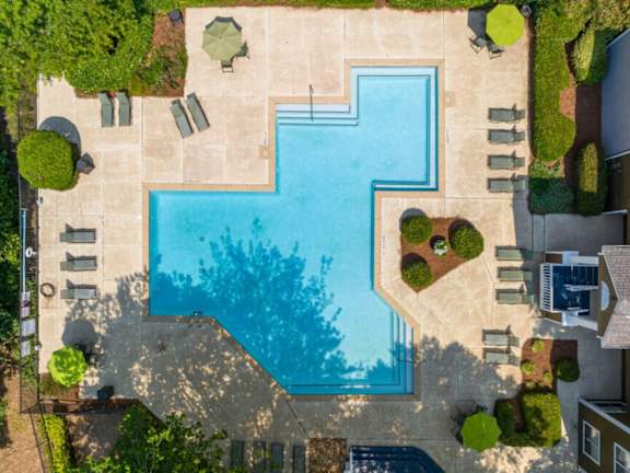 A large swimming pool surrounded by a concrete patio and green bushes.