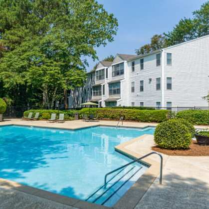 A swimming pool surrounded by trees and a building in the background.