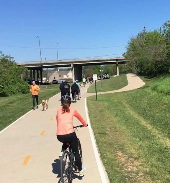 A woman riding a bike on a path with a group of people and a dog following behind.
