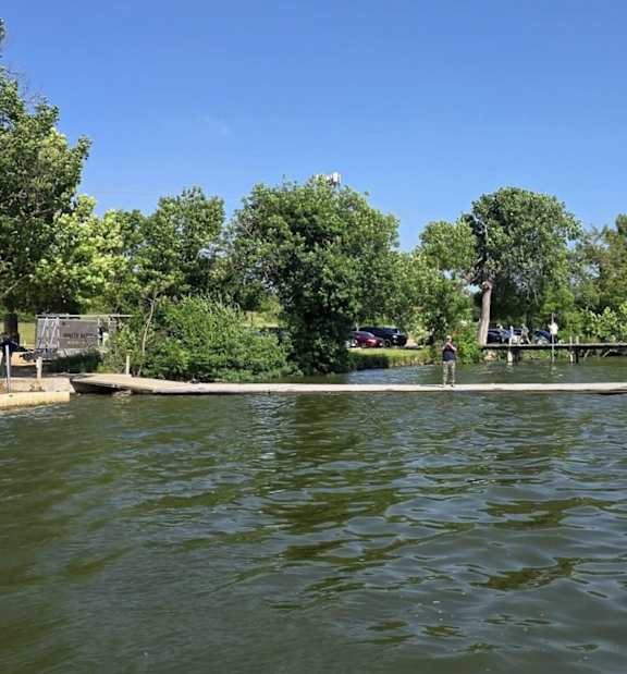 A serene lake surrounded by lush green trees under a clear blue sky.