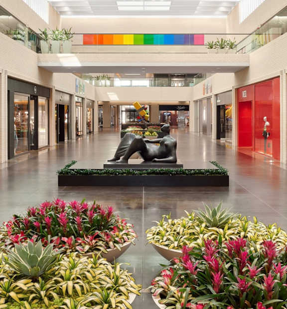 A shopping mall with a statue in the middle of a planter.