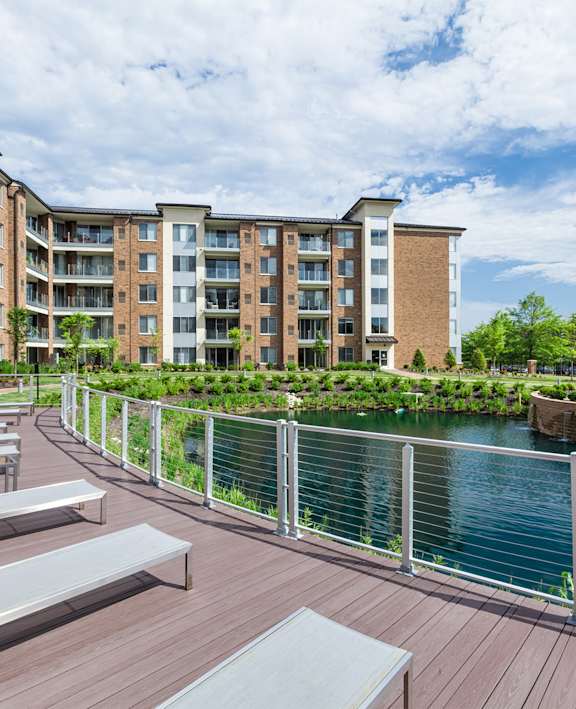 A modern apartment complex with a wooden deck and benches overlooking a body of water.