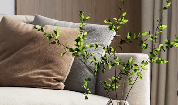 a couch with two pillows and a plant in a vase