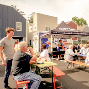 people sitting at picnic tables in front of food trucks in a parking lot