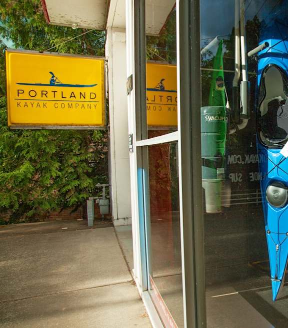 A storefront of the Portland Kayak Company with kayaks displayed in the window.