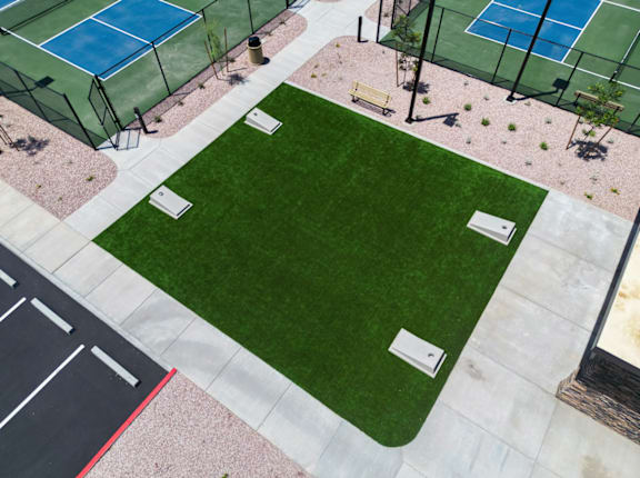 A tennis court surrounded by a fence and a green lawn.