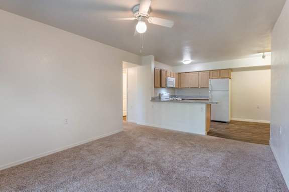 View from Carpeted Living Room of Breakfast Bar off Kitchen with Blonde Cabinets Grey Counters and White Appliances