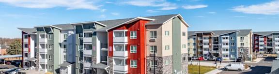 A row of modern apartment buildings with cars parked in the lot.