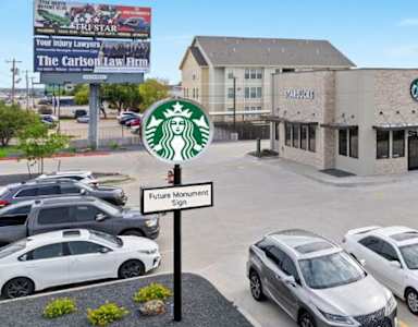 A Starbucks sign is in front of a building with a parking lot in front of it.