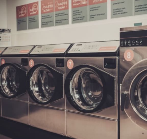 A basket of clothes is placed in front of a row of washing machines.